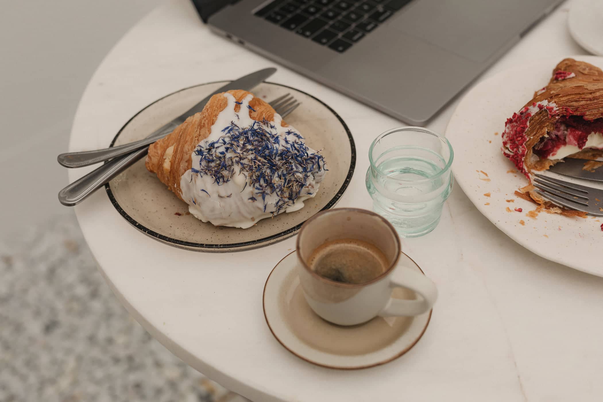 Espresso, pastries and an open laptop on a round marble café table