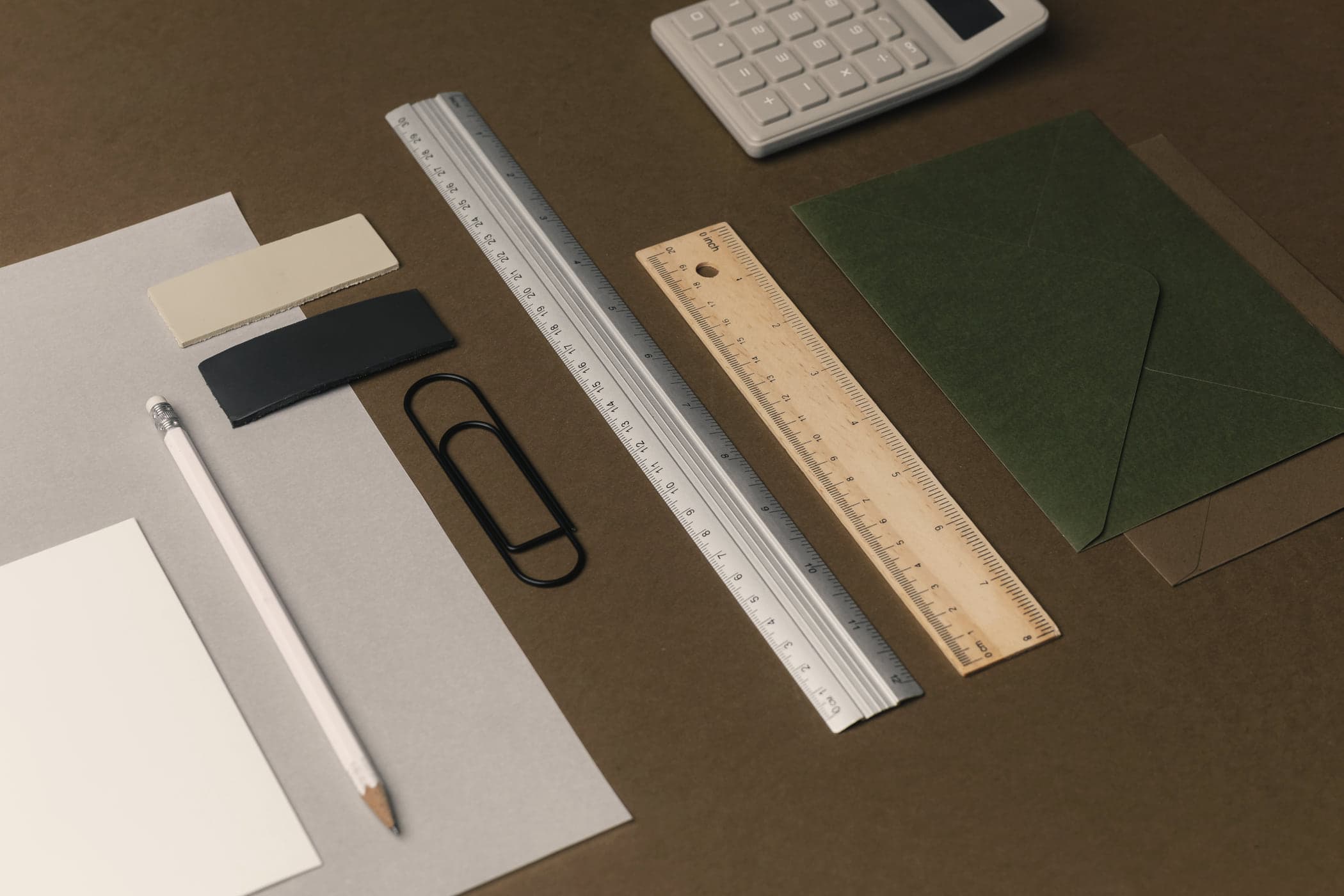 A ruler, paper clip, pencil and calculator laid out neatly on an olive desk