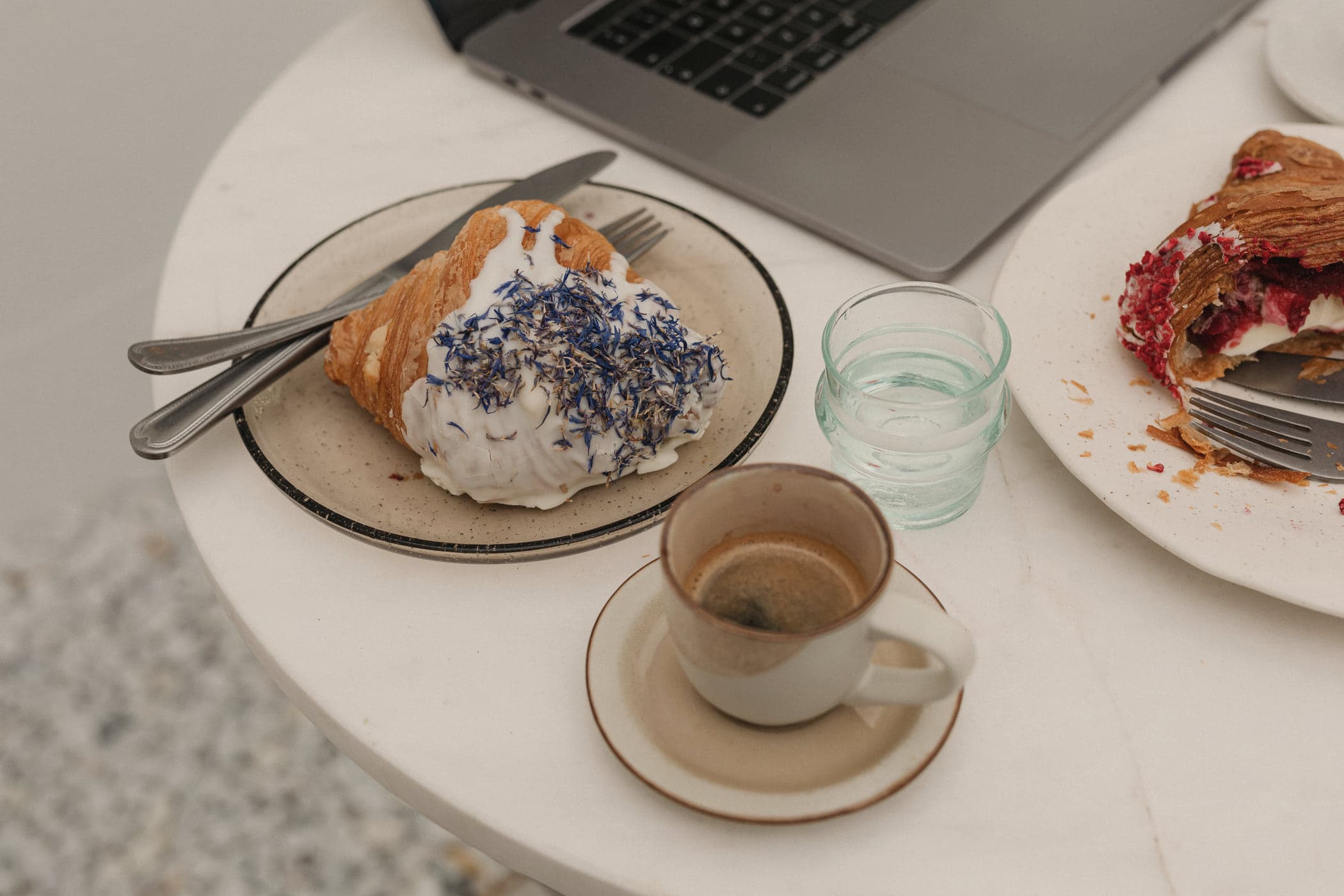 Espresso, pastries and an open laptop on a round marble café table